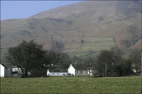 House dwarfed by a hill with dry stone walls up it's side